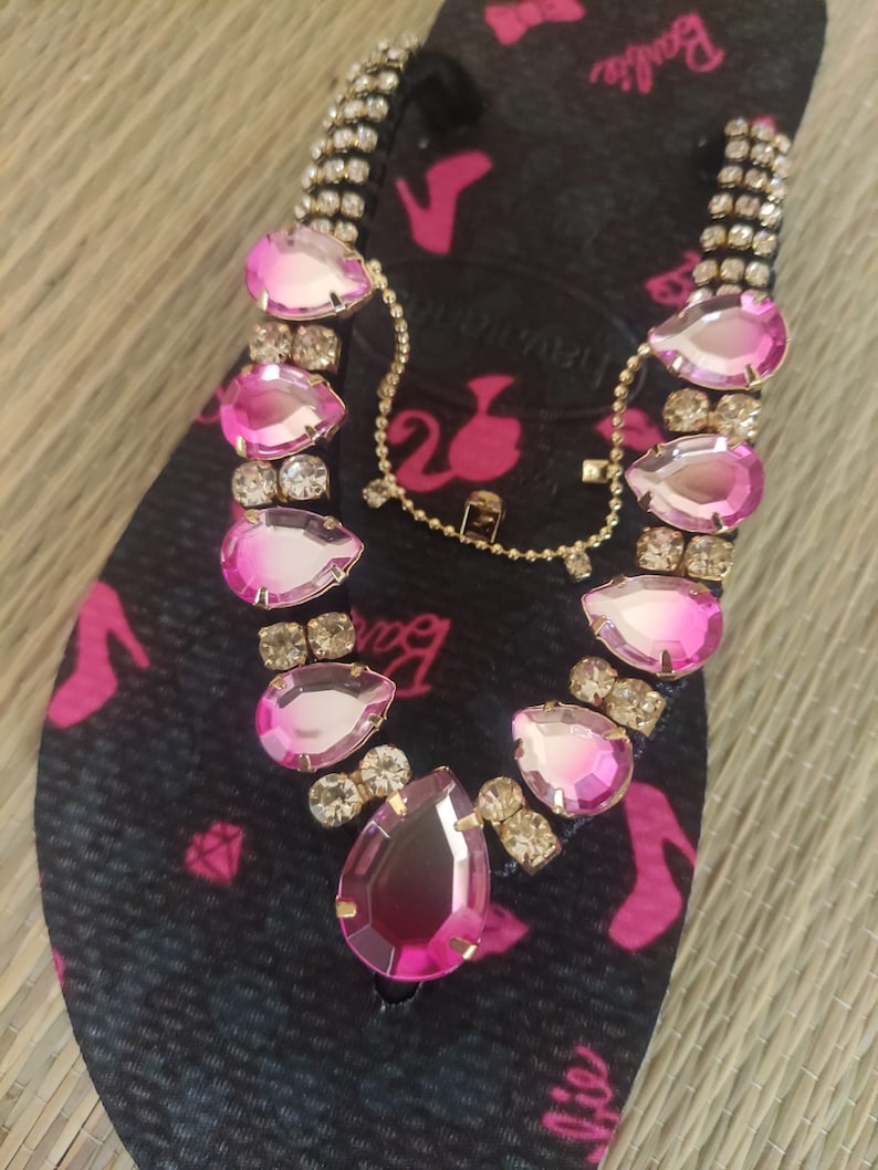 May include: Black flip-flops with a pink Barbie logo and pink and clear rhinestone embellishments.