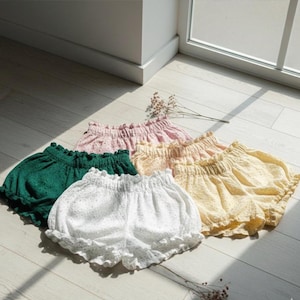 Può includere: Una collezione di cinque paia di culotte in bianco, verde scuro, rosa chiaro, pesca e giallo. Ogni paio presenta un girovita elasticizzato con volant, una vestibilità ampia e un tessuto in pizzo sangallo con motivi traforati.