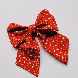 May include: A red fabric bow with white stars printed on it. The bow is tied in a large, loose knot.