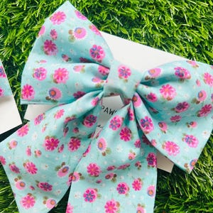 May include: A large, light blue bow with a pink floral pattern. The bow is made of fabric and has a simple design.