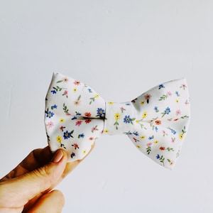 May include: A white bow tie with a small floral pattern in shades of pink, blue, yellow, and green.