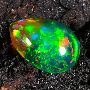 May include: A pear-shaped loose gemstone featuring a translucent body with a vibrant play-of-color. The stone displays intense flashes of neon green, bright orange, and electric blue, creating a multi-colored iridescent effect across its surface.