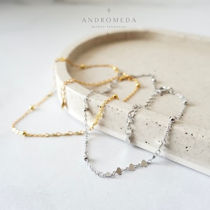 May include: Two delicate chain bracelets with small heart charms and beads. One bracelet is gold and the other is silver.