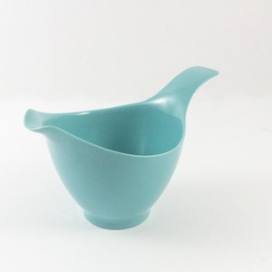 May include: A light blue ceramic pitcher with a curved spout and a handle. The pitcher is designed in a bird shape.