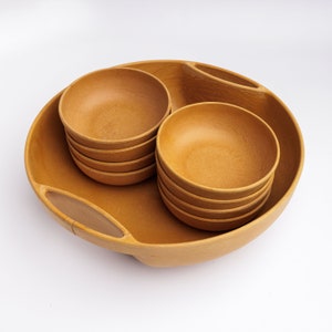 May include: A set of brown wooden bowls, including a large serving bowl with two handles and four smaller bowls stacked inside. The bowls are made of natural wood and have a rustic, earthy look.