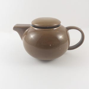 May include: A brown ceramic teapot with a round body and a lid. The teapot has a handle on the side.