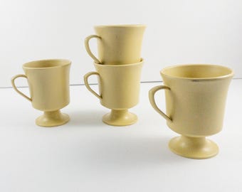 May include: Set of four yellow ceramic coffee mugs with a pedestal base. The mugs are stacked on top of each other.