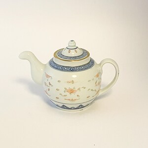 May include: A white porcelain teapot with a lid, spout, and handle. The teapot is decorated with blue and orange floral patterns and a gold rim. The base and lid have blue geometric designs.