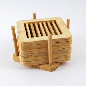 May include: A set of six natural bamboo coasters with a slatted design. The coasters are stacked and held together by four vertical bamboo sticks.