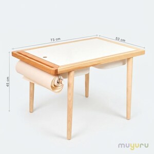 May include: A wooden art table with a white surface and a roll of paper. The table is 28.7 inches long, 20.9 inches wide, and 17.7 inches high. The table has a natural wood frame and legs, and a built-in paper roll holder.