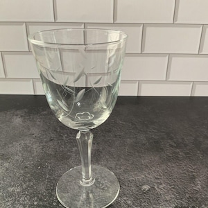 May include: A white ceramic mug with a black handle and the text "But First, Coffee" in a bold, black font. The mug is set against a blurred background, suggesting a cozy setting.