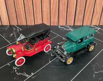以下が含まれることがあります： ヴィンテージスタイルのモデルカー2台。1台は黒い屋根と白い縁取りのホイールを備えた赤いオープンカー。もう1台は黒いフェンダーと黄色い縁取りのホイールを備えた緑色のクローズドカーで、どちらも金属製のアクセントと詳細なフレームが特徴です。