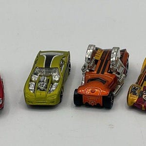 Könnte beinhalten: Sechs Spielzeugautos in verschiedenen Farben, darunter Burgunderrot, Rot, Limettengrün, Orange, Gold und Weiß. Jedes Auto hat einzigartige Designs, mit sichtbaren Motordetails und Rennstreifen. Kleine Modellautos.
