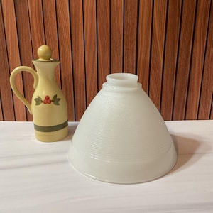 Op de afbeelding: Een gele keramische oliekan met een handvat, een deksel en een decoratief bessen- en bladerontwerp. Daarnaast een witte, getextureerde glazen lampenkap met een brede basis en een smalle bovenkant.