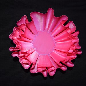 Könnte beinhalten: Eine rosa, 3D-gedruckte Schale mit einem gekräuselten Rand. Die Schale ist aus glattem, glänzendem Kunststoff.
