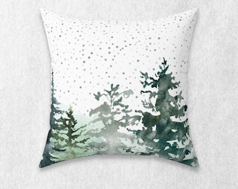 May include: A white throw pillow with a watercolor design of a forest scene. The trees are green and blue, and there are white dots scattered across the background.