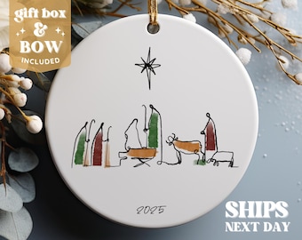 May include: White ceramic ornament with a black line drawing of the nativity scene. The drawing includes a star, a manger, a cow, a donkey, and several figures. The year 2025 is written at the bottom of the ornament.