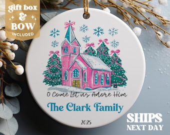 May include: A pink church with white trim and snow on the roof, surrounded by green trees with white lights. The text "O Come Let us Adore Him" and "The Clark Family" is printed below the church. The year 2025 is printed at the bottom of the ornament.