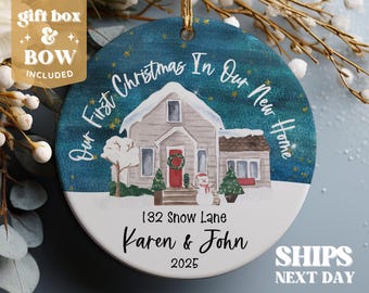 Peut inclure: Ornement de Noël rond avec une scène hivernale d'une maison, de neige et d'arbres. Le texte indique "Our First Christmas In Our New Home", "132 Snow Lane, Karen & John, 2025". Comprend une boîte cadeau et un nœud.