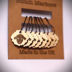 May include: A set of 10 wooden stitch markers featuring a sheep design. The markers are brown and have a metal loop. The card reads "Stitch Markers" and "Made in the UK".