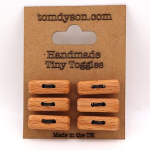 May include: Six handmade wooden toggles with black cord loops are displayed on a brown card. The card reads "tomdyson.com" and "Handmade Tiny Toggles." The bottom of the card says "Made in the UK."