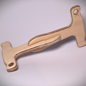 May include: A wooden craft tool with a light brown finish. The tool has a unique shape with a handle, a curved section, and a small hole at each end. The edges of the wood are a darker brown.
