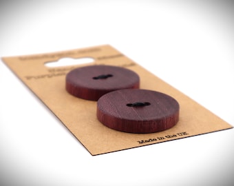 May include: Two round, dark burgundy wooden buttons with black thread, displayed on a brown cardboard backing. The buttons are handmade and have a smooth finish. The packaging reads "Made in the UK."