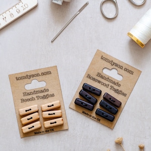 Peut inclure: Vue aérienne de fournitures de couture, dont deux ensembles de toggles en bois faits à la main, un en hêtre et un en palissandre, sur un emballage en carton. Le texte "tomdyson.com" et "Made in the UK" sont visibles. Une règle, des ciseaux, du fil et une aiguille sont également présents.