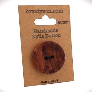 May include: A 40mm handmade Xylia button on a brown card. The button is a dark brown colour with a visible wood grain pattern. The card features the text "tomdyson.com" and "Handmade Xylia Button". Made in the UK.