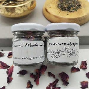 Puede incluir: Dos pequeños frascos de vidrio con tapas blancas que contienen incienso. El frasco de la izquierda está etiquetado como "Incenso Meditanico Meditaizone - Viaggi astrali - Sogn", y el frasco de la derecha está etiquetado como "Incenso per Purificazione".