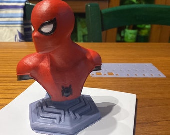 May include: A red and black 3D printed bust of Spider-Man with a detailed face and a black spider logo on the chest. The bust is mounted on a blue and gray base with a geometric design.