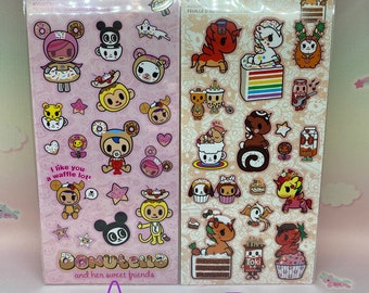 May include: Two vertical sheets of Tokidoki stickers featuring Donutella and her sweet friends. Sheet A is light pink with various cartoon characters and the text 'I like you a waffle lot!' and 'Donutella and her sweet friends'. Sheet B is beige.