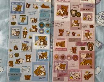 May include: Two sheets of sticker paper featuring Rilakkuma, a popular Japanese bear character. The stickers are on a pink and blue background and feature various images of Rilakkuma and his friends. The text on the stickers reads "Memory Frame Seal" and "Rilakkuma".