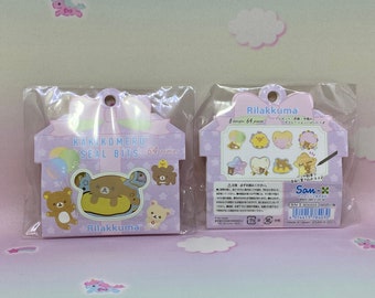 May include: Two packages of Rilakkuma seal bits. The packaging is light purple with bear illustrations. Text reads "KAKIKOMERU SEAL BITS 64 pieces". The back of the package shows 8 different designs. The product is made in Japan.
