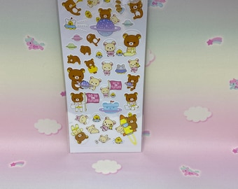 May include: A sheet of Rilakkuma space-themed stickers featuring a brown bear in various poses, including flying in a spaceship, holding a flag that says "Go to Future", and riding a rocket. The stickers are on a white background with a blue and purple gradient.