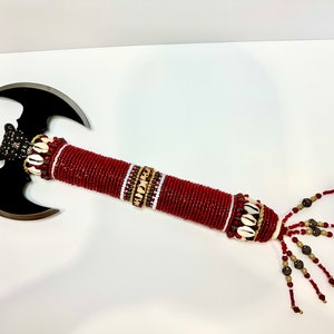 May include: A black double-headed axe with a red beaded handle and white and brown accents. The handle has a tassel of red, white, and brown beads.