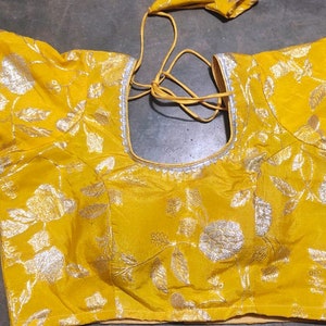 May include: A yellow blouse with silver floral embroidery and a silver trim around the neckline and sleeves.