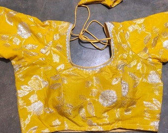 Puede incluir: Una blusa amarilla con bordados florales plateados y un ribete plateado alrededor del escote y las mangas.