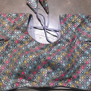 May include: A blue, pink, and gold embroidered blouse with a geometric pattern. The blouse has long sleeves and a round neckline. The blouse has a tie at the back.