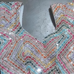 Puede incluir: Un top de tela blanca con un patr&oacute;n de chevron colorido hecho de lentejuelas. Las lentejuelas son en tonos de rosa, naranja, amarillo, verde, azul y morado.