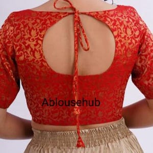 May include: Red brocade blouse with a keyhole back and a gold floral pattern. The blouse has short sleeves and ties at the back.