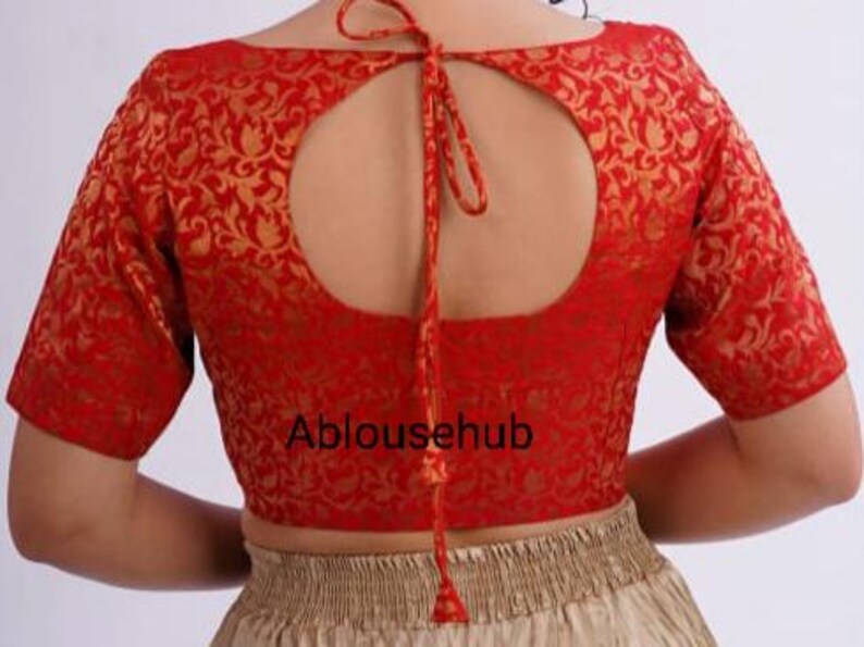 May include: Red brocade blouse with a keyhole back and a gold floral pattern. The blouse has short sleeves and ties at the back.