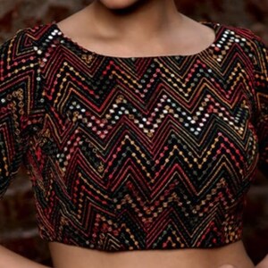 May include: A black top with a zig-zag pattern in red, gold, and white. The top has a scoop neckline and short sleeves. The design is made with sequins and embroidery.