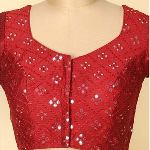 May include: A maroon silk blouse with a geometric pattern and mirror embellishments. The blouse has a scoop neckline and short sleeves.