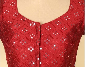May include: A maroon silk blouse with a geometric pattern and mirror embellishments. The blouse has a scoop neckline and short sleeves.