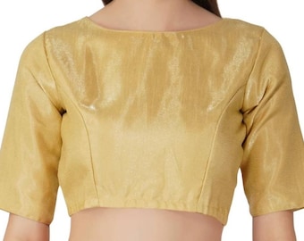 Puede incluir: Una blusa dorada con cuello barco y mangas hasta el codo. La tela tiene un brillo sutil, lo que le da un aspecto lujoso. La blusa es de color liso y parece estar hecha de un material suave, posiblemente similar a la seda.
