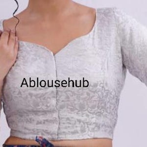 May include: A white, short-sleeved blouse with a floral pattern and a V-neckline. The blouse is made of a soft, silky fabric. The text "Ablousehub" is printed on the front of the blouse.