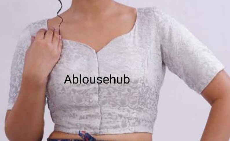May include: A white, short-sleeved blouse with a floral pattern and a V-neckline. The blouse is made of a soft, silky fabric. The text "Ablousehub" is printed on the front of the blouse.