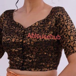 May include: A black and gold brocade blouse with a V-neckline and short sleeves. The blouse has a button closure at the front and a floral pattern.