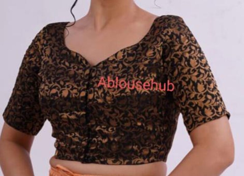 May include: A black and gold brocade blouse with a V-neckline and short sleeves. The blouse has a button closure at the front and a floral pattern.